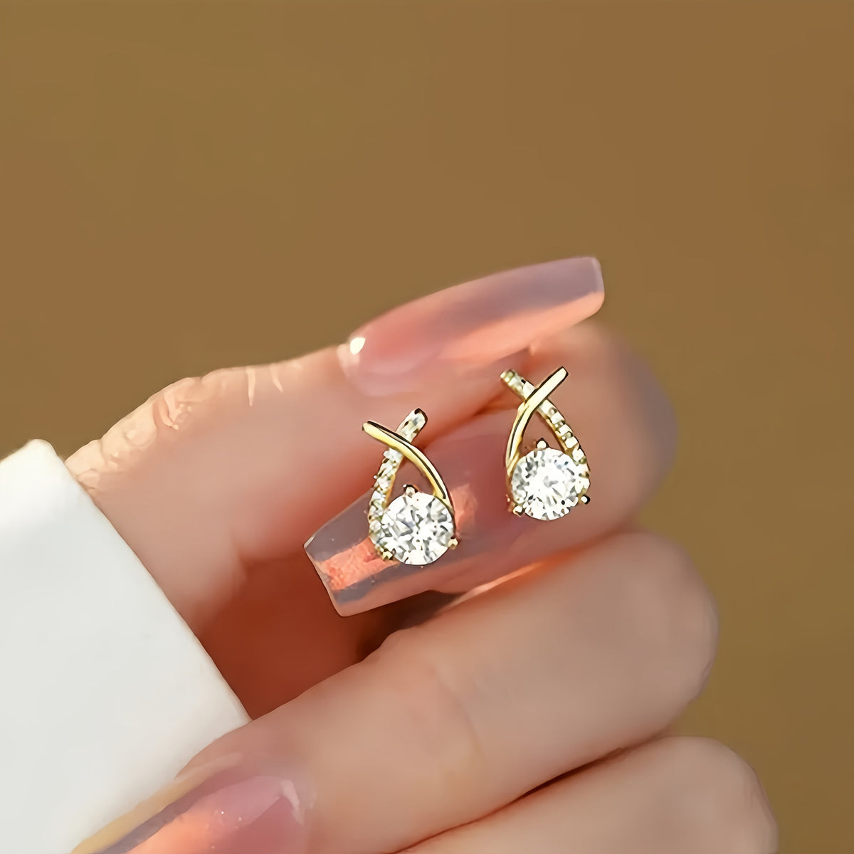 Leni gold cross earrings held in hand, detail view