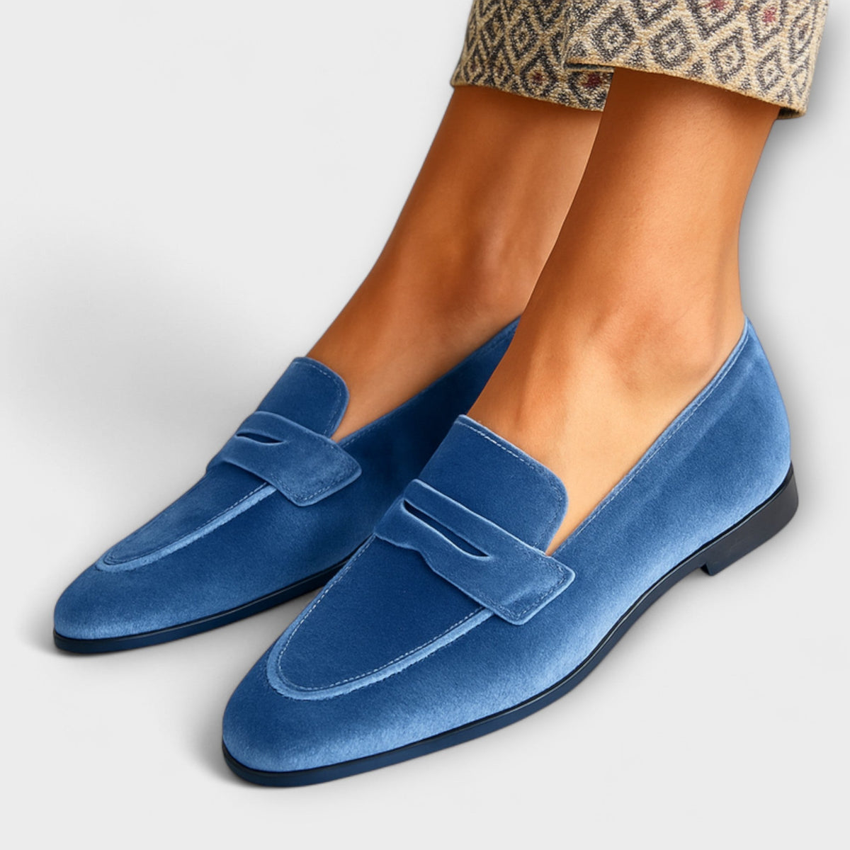 Monica velvet penny loafers in blue, worn side view with patterned trousers