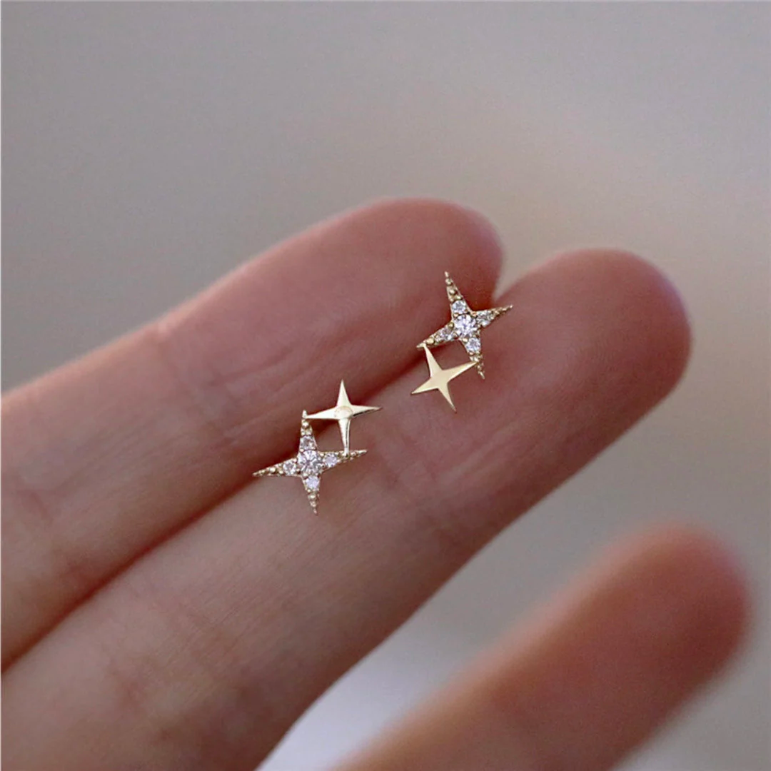 Shimmering star gold stud earrings in gold, close-up held on fingertips