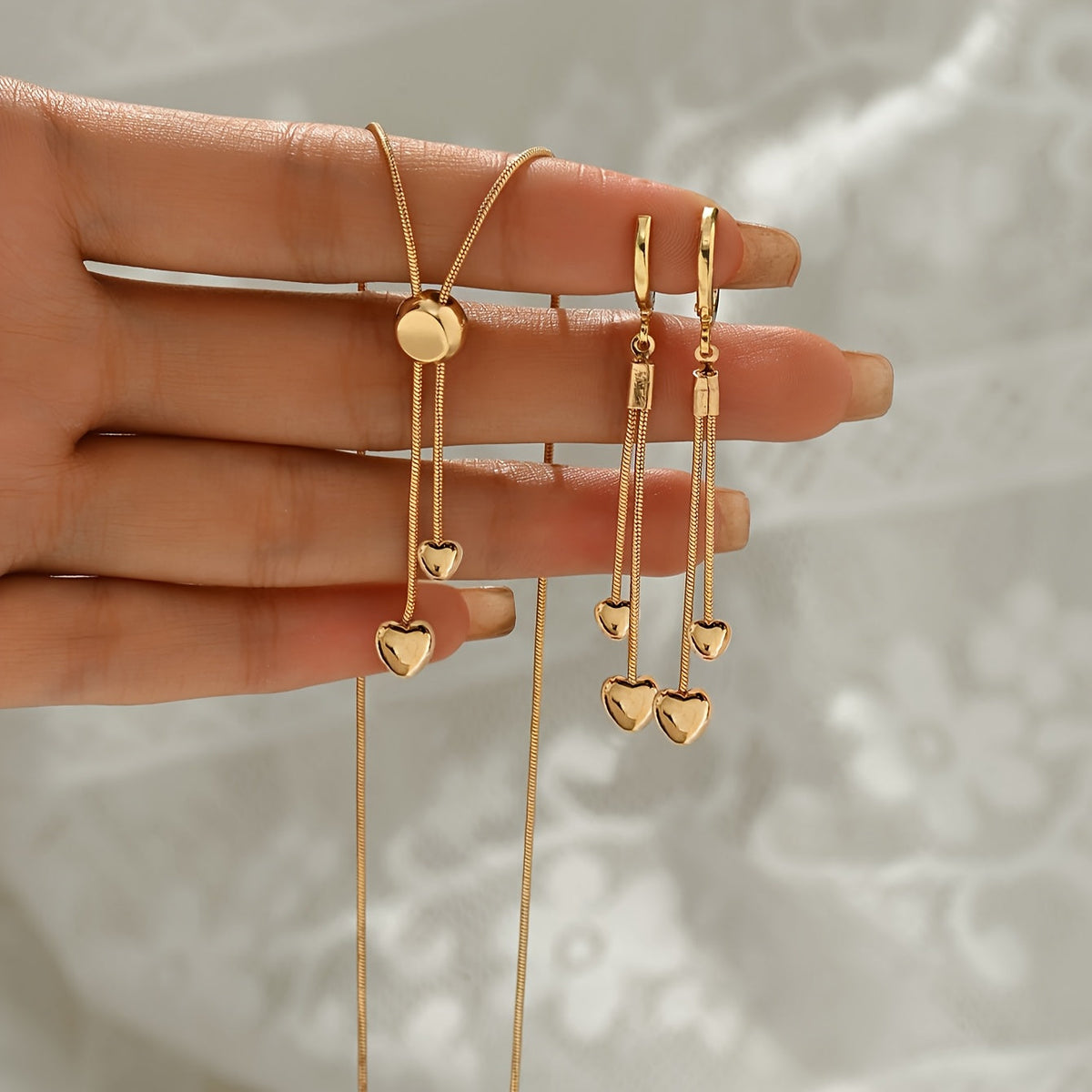 Gold heart jewellery set held in hand, showing chain and earring drops