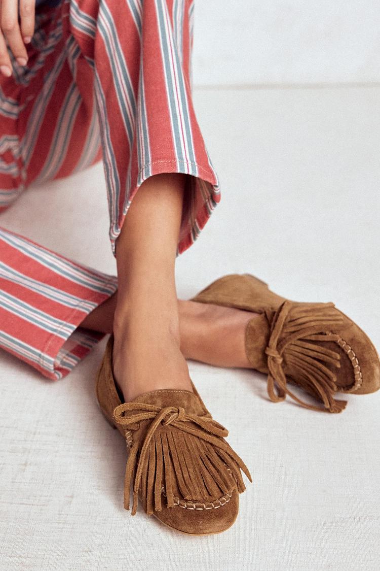 Camel round-toe fringed loafers worn with striped trousers, seated side view