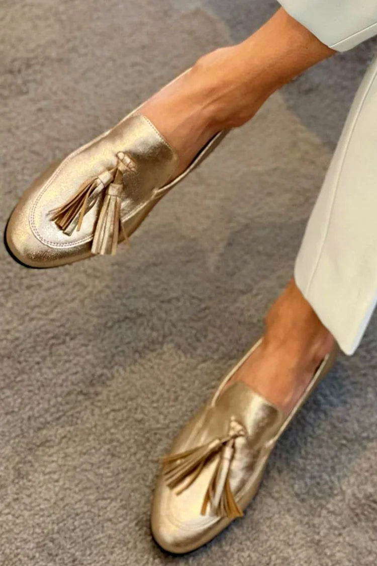 Gold metallic loafers with tassels, worn with cream trousers, close front view