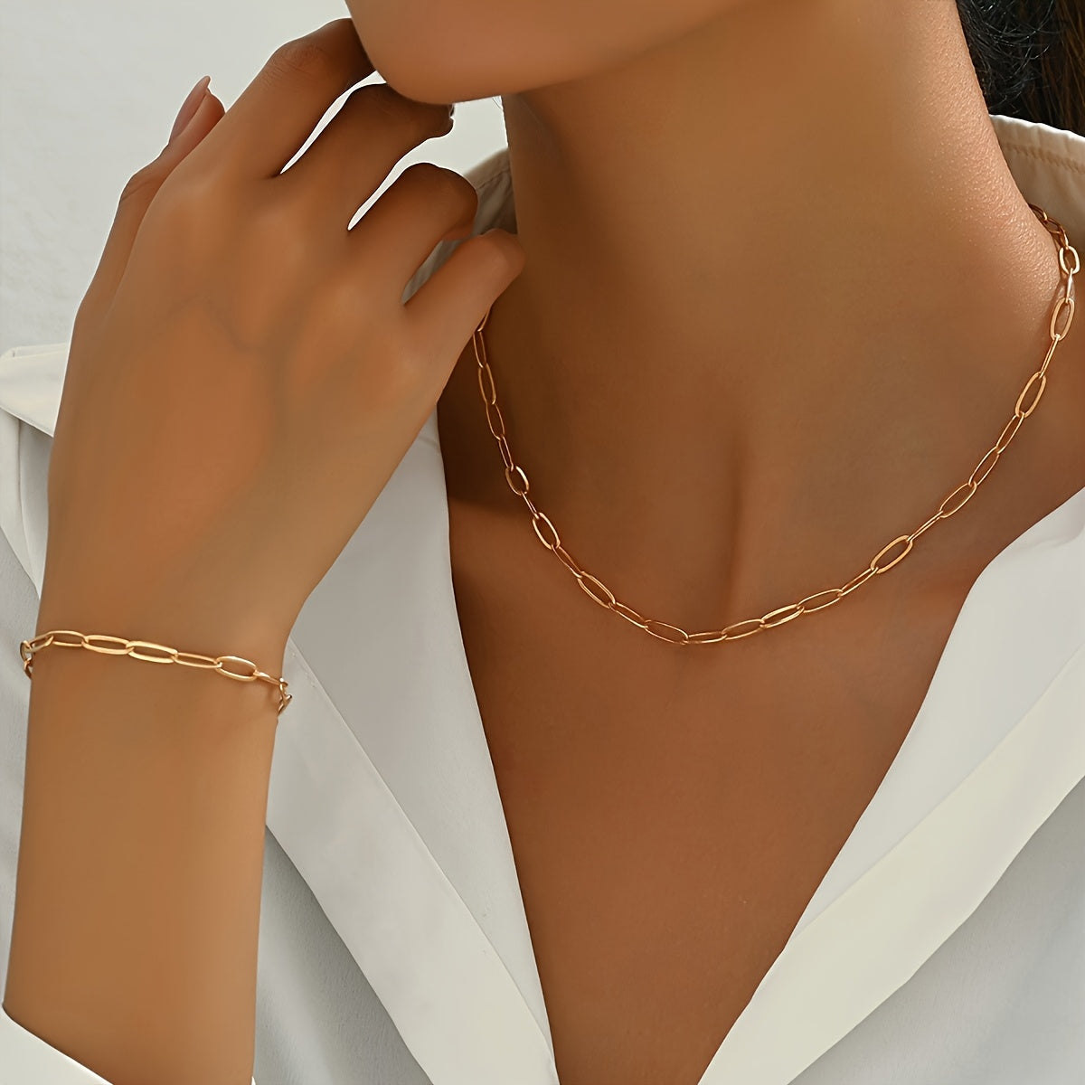 Gold paperclip-link necklace and bracelet worn with a white collared shirt