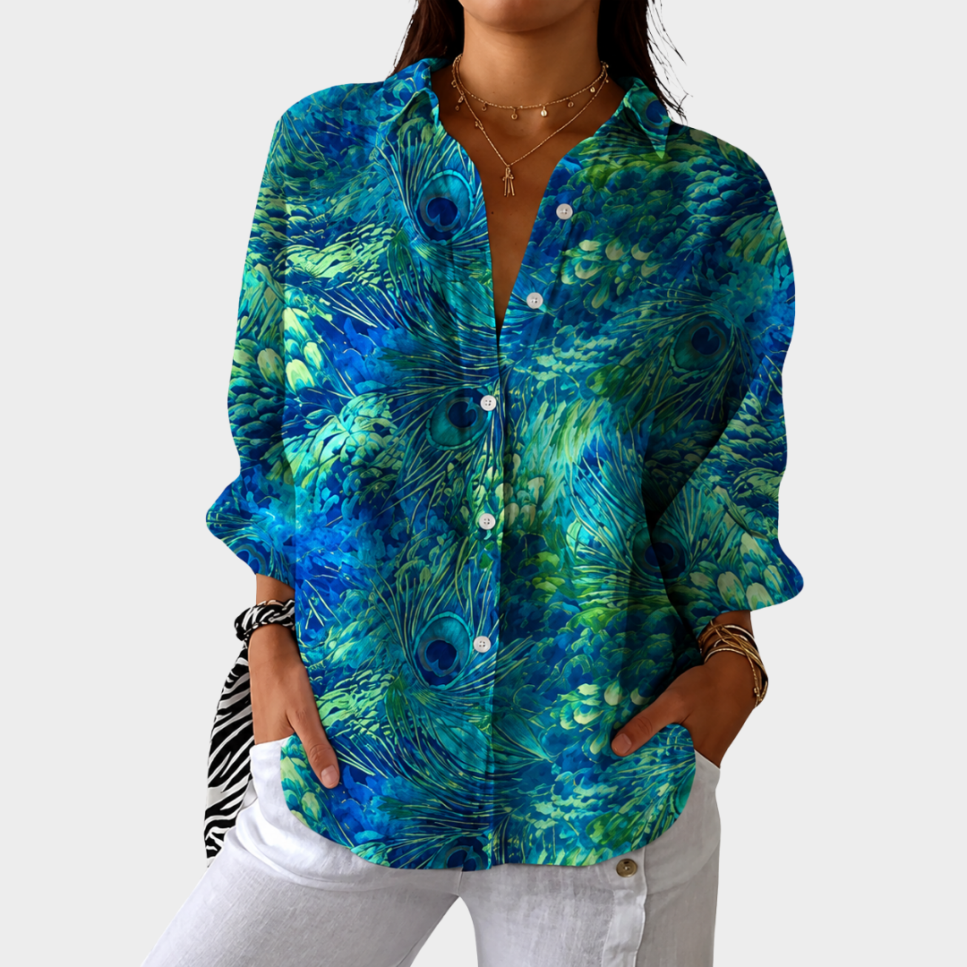 Printed blouse in blue and green peacock feather print, front view with white trousers