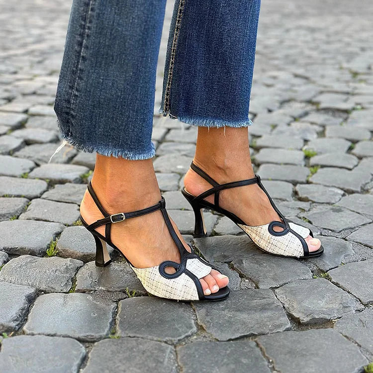 White and black T-bar stiletto sandals, three-quarter view on a cobbled street
