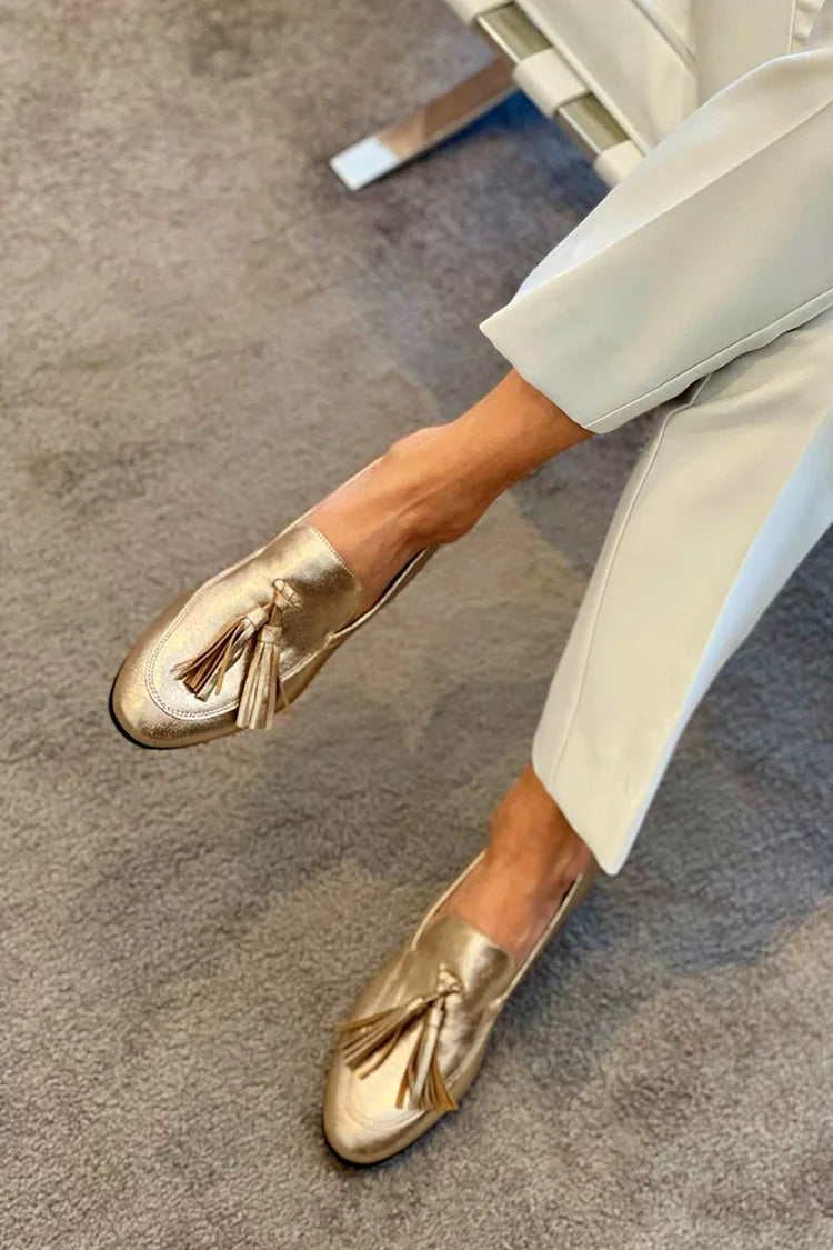 Gold metallic tassel loafers in gold, seated side view with cream trousers