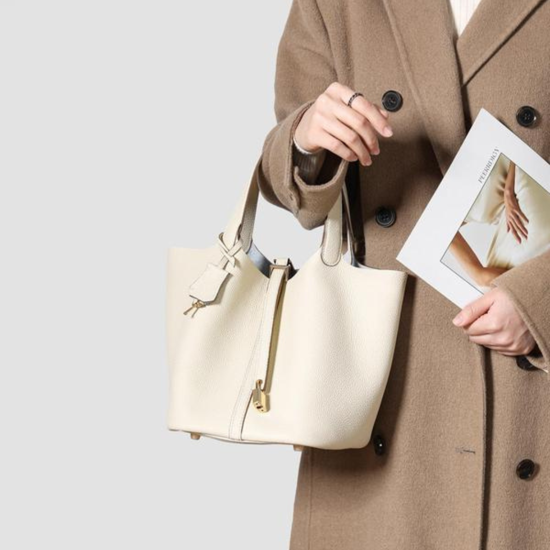 Kate lock bag in off-white, held by a model in a camel coat