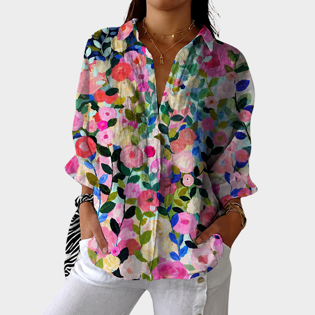 Colourful painted floral print lightweight blouse worn open over white trousers, front view