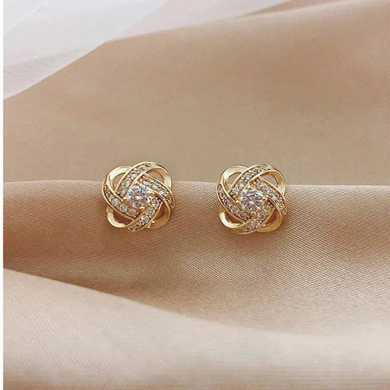 Floral spiral knot stud earrings in gold, close-up on fabric