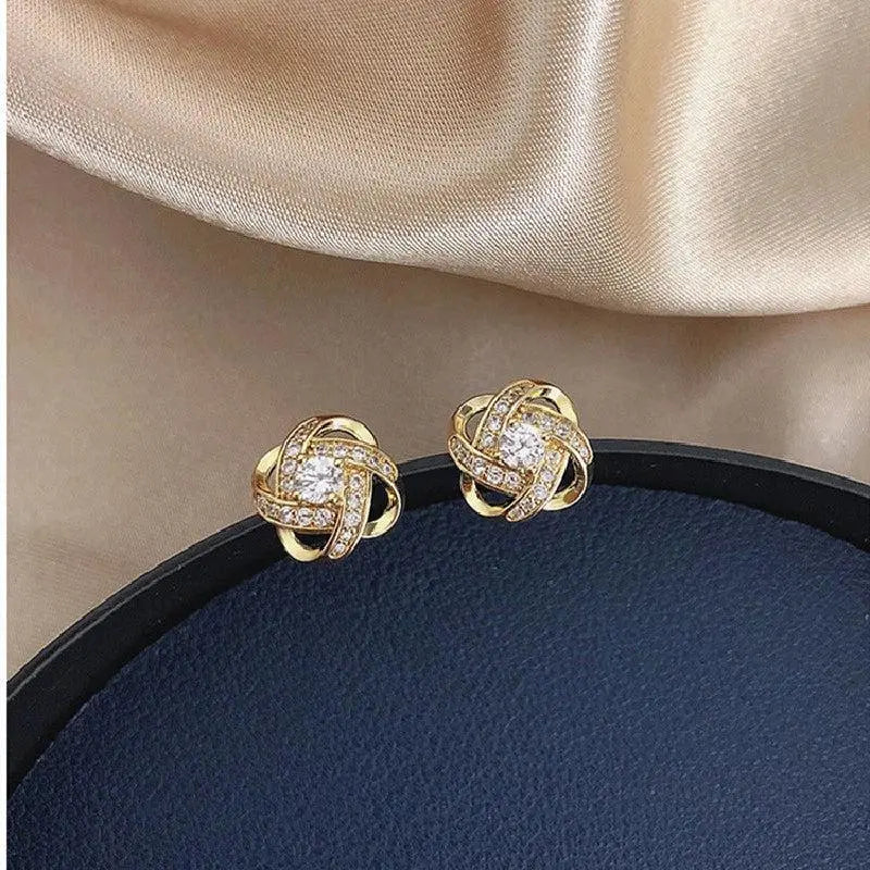 Gold floral spiral stud earrings resting on a dark tray, angled view