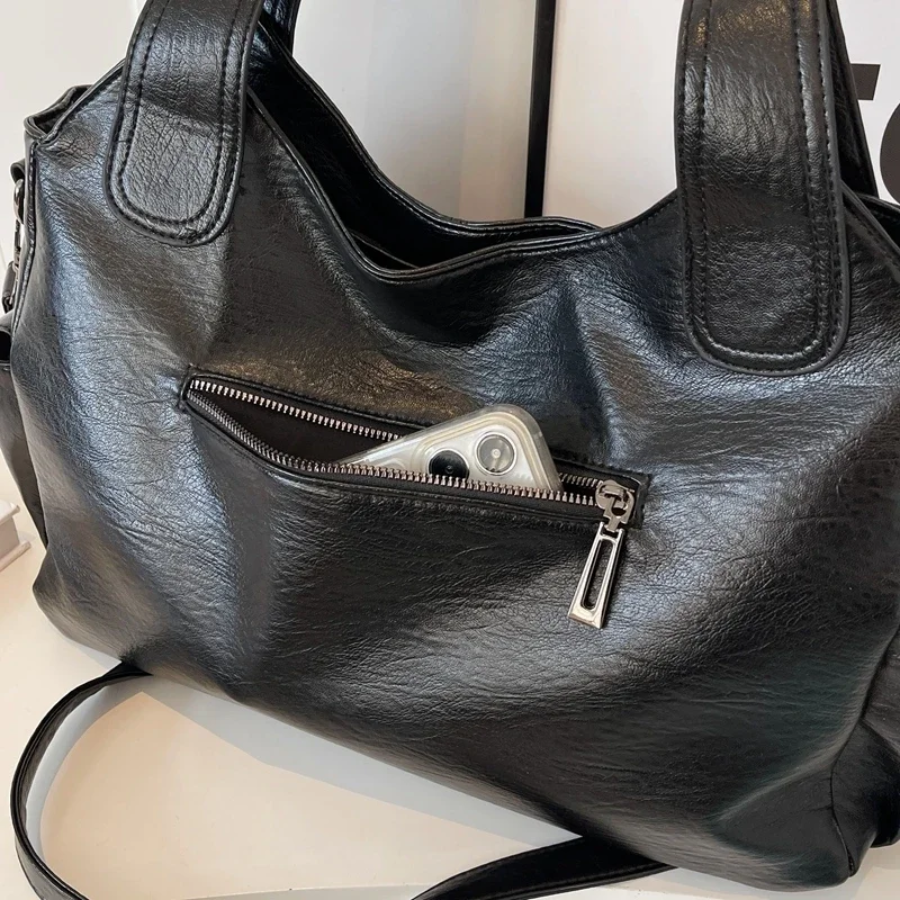 Close-up of black shoulder bag zip pocket holding a phone