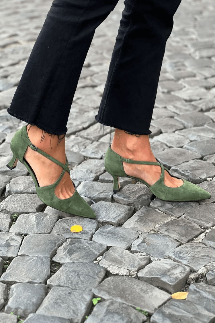 Green suede pointed-toe kitten heels with cross straps, worn with black cropped jeans