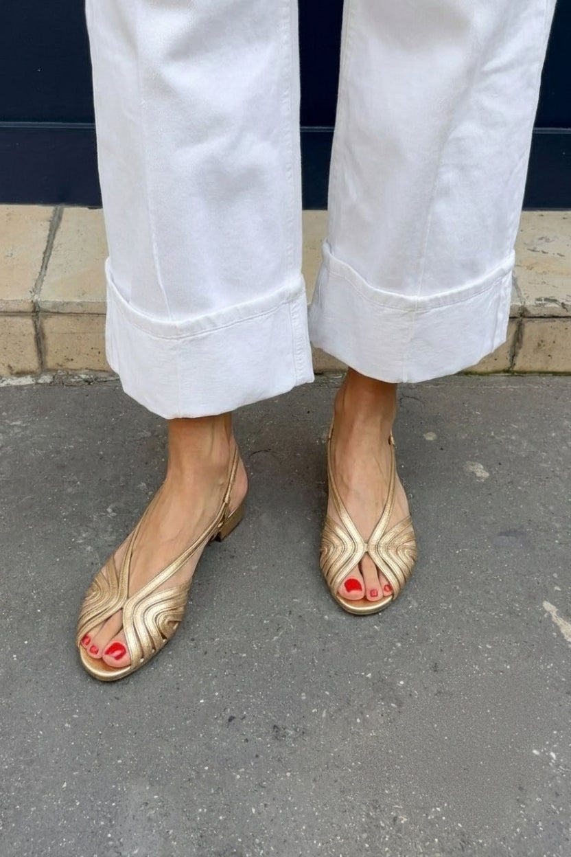 Gold metallic round-toe slingback sandals worn with white wide-leg trousers, front view