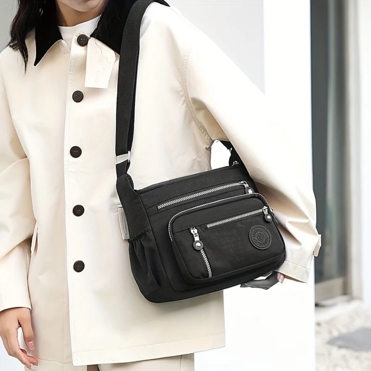 Evelisse shoulder bag in black worn crossbody over a cream jacket