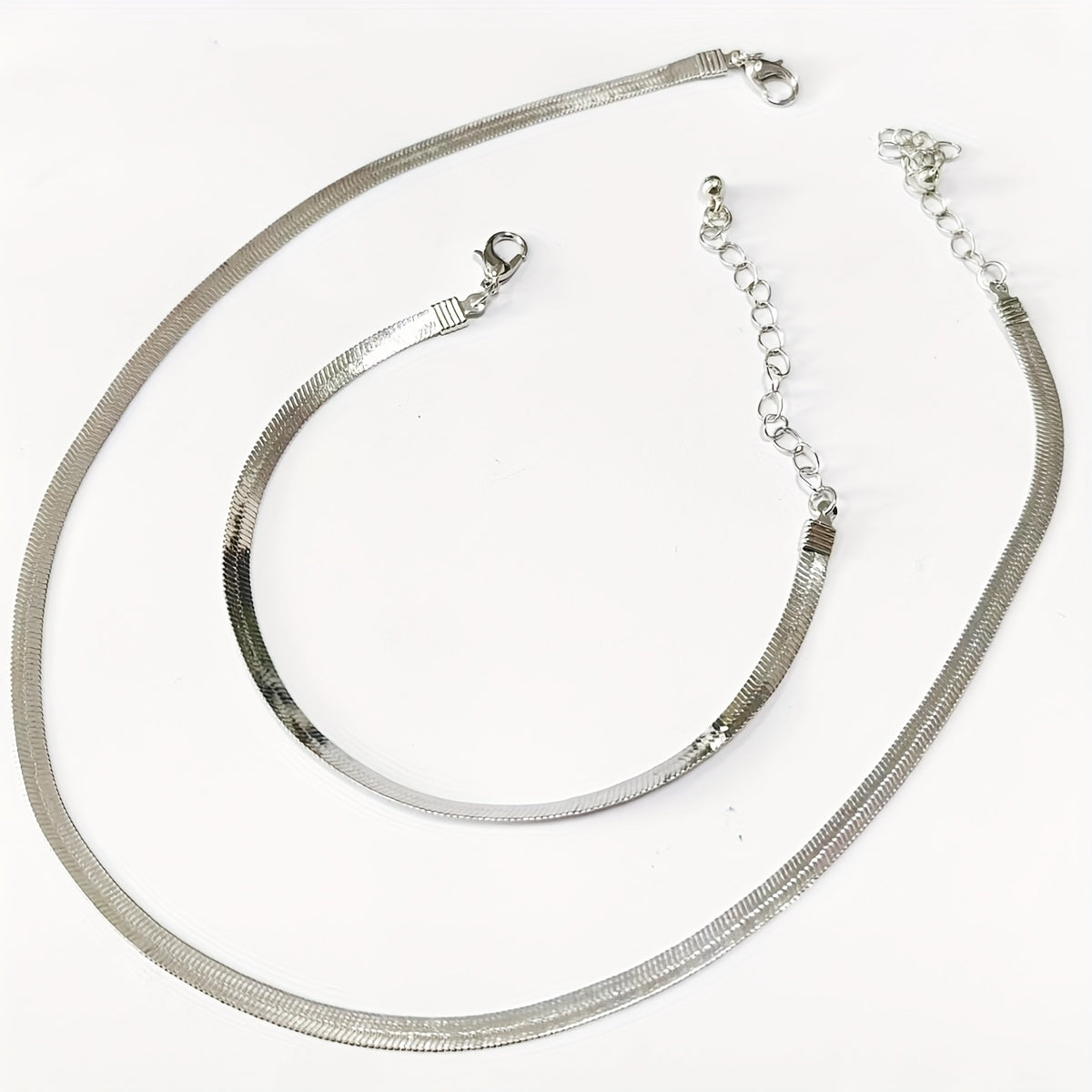 Silver flat snake chain necklace and bracelet laid flat with clasps visible