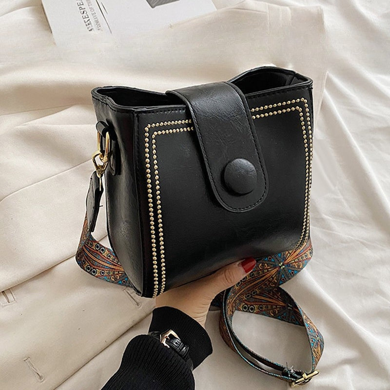 Ethel shoulder bag in black held in hand, showing wide patterned strap