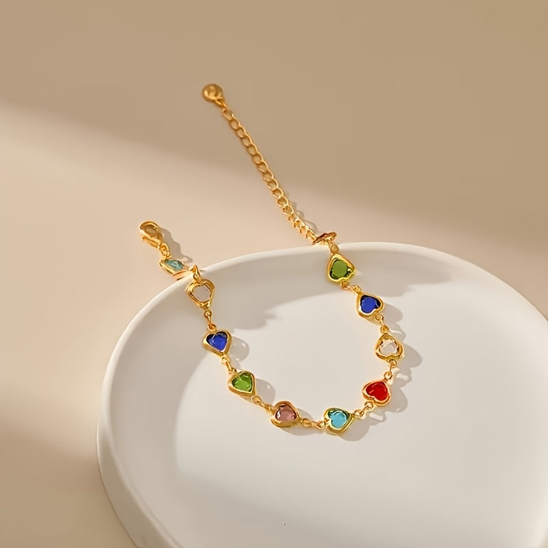 Gold heart bracelet with rainbow stones resting on a white dish