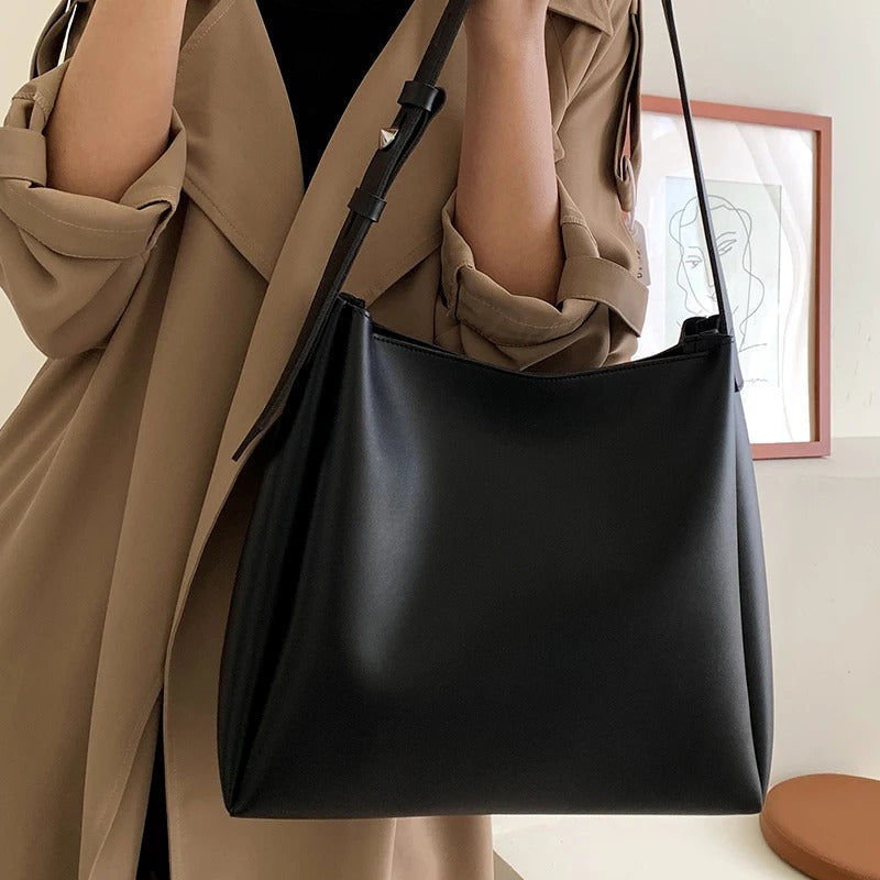 Delphine grand tote in black worn over the shoulder with a trench coat