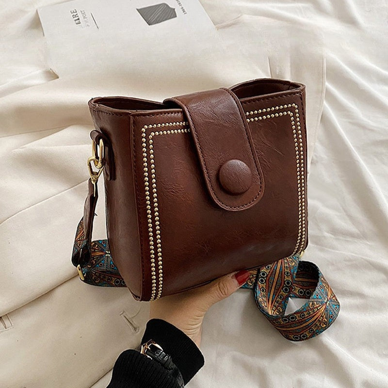 Ethel shoulder bag in coffee held in hand, close view of dome button tab