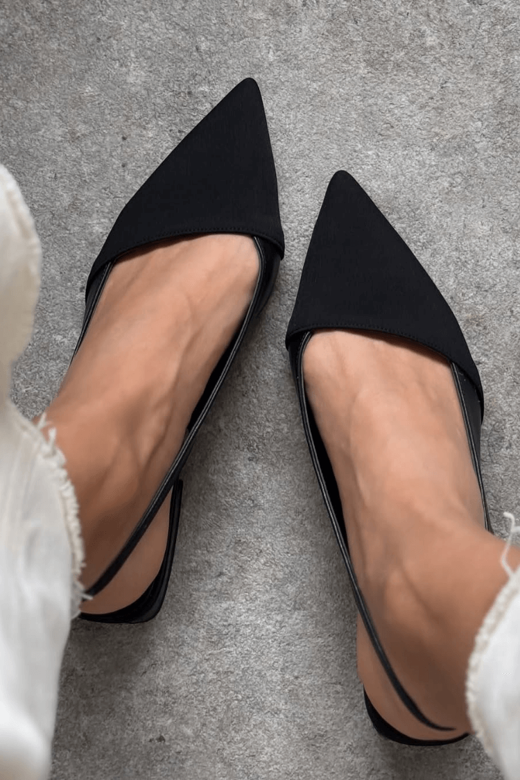 Black slingback ballet flats with pointed toes, top-down view on model