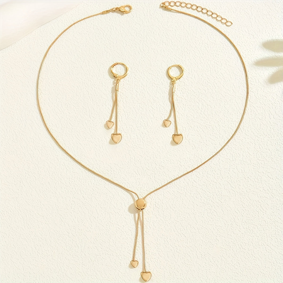 Gold heart necklace with sliding pendant and matching earrings laid flat