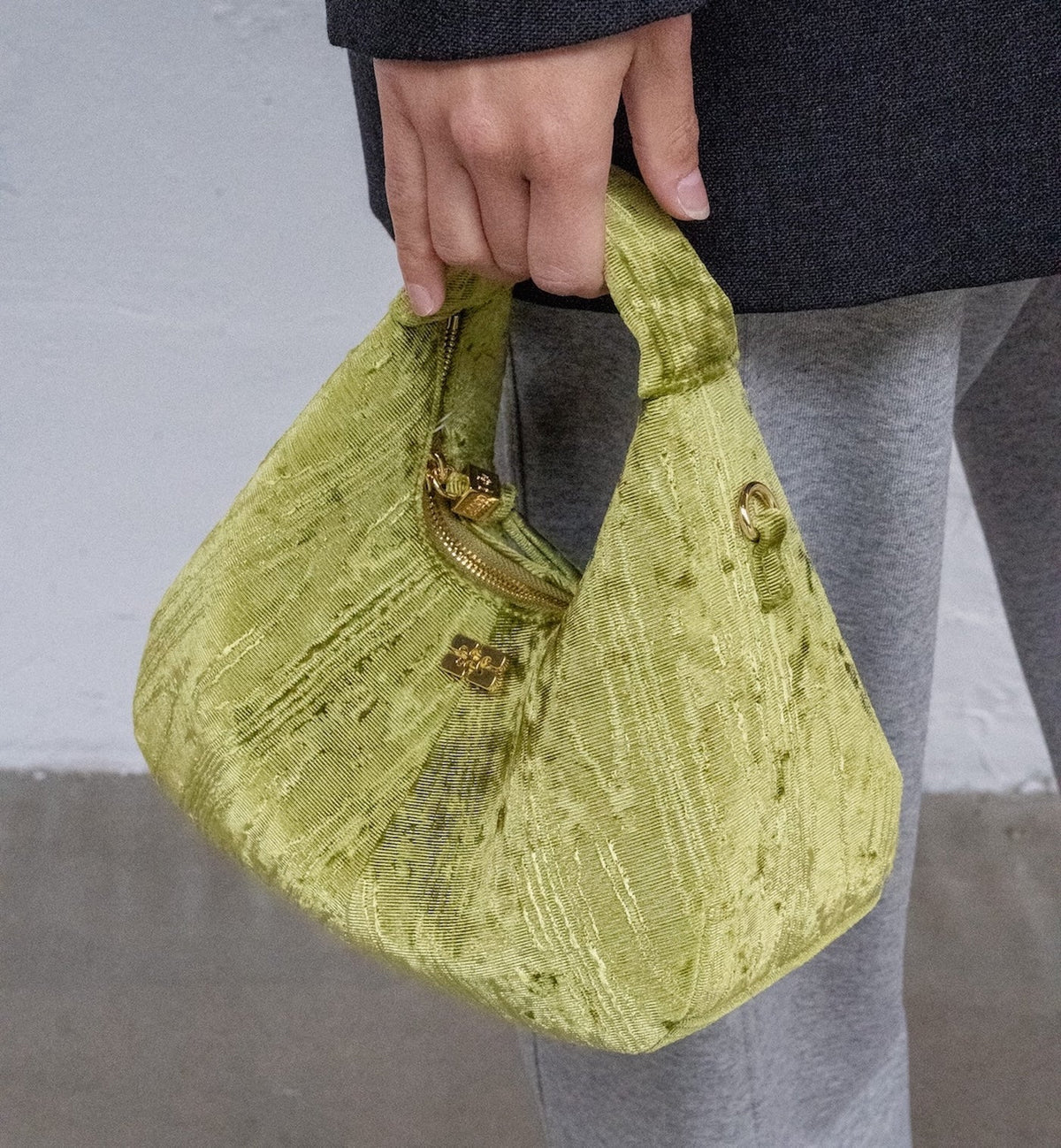 Close-up of Roma Luxe green mini bag showing gold zip and logo plaque