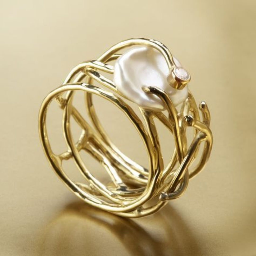 Gold woven band ring with white pearl and small clear stone, angled view