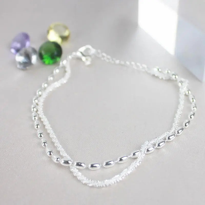 Silver zirconia and bead bracelet set shown flat beside coloured gemstones