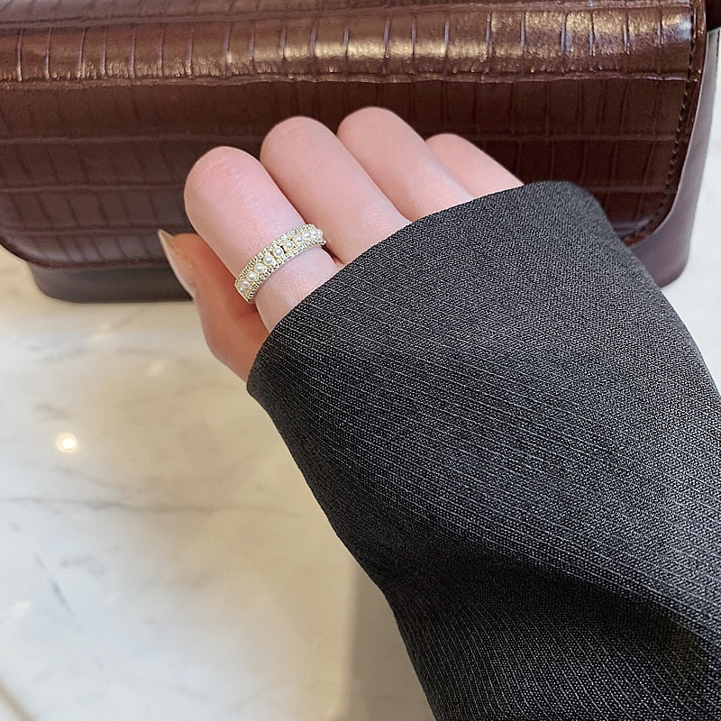 Gold and pearl ring worn on the finger with a dark blazer sleeve