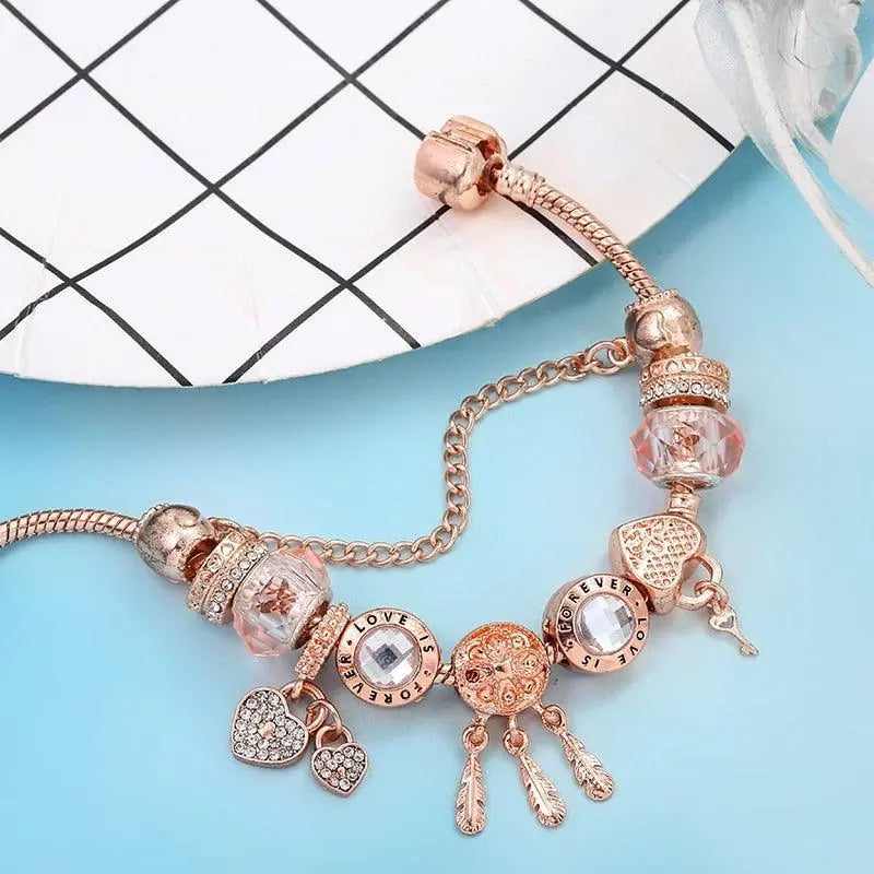 Rose gold charm bracelet with engraved love beads on a blue background