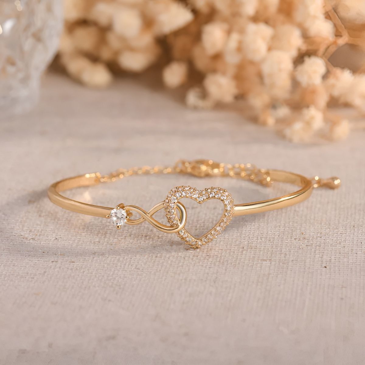 Endless Love gold bracelet on linen with dried flowers behind