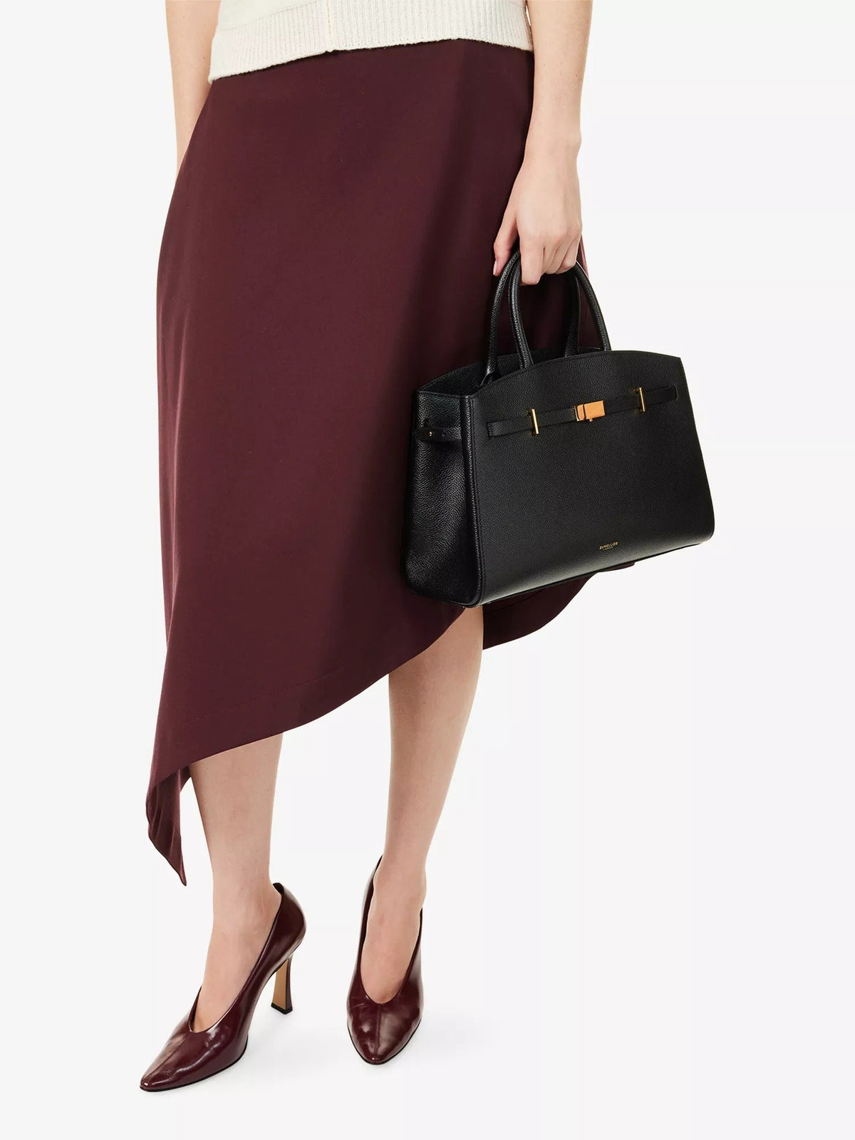 Amélisse midi handbag in black carried by hand with burgundy skirt