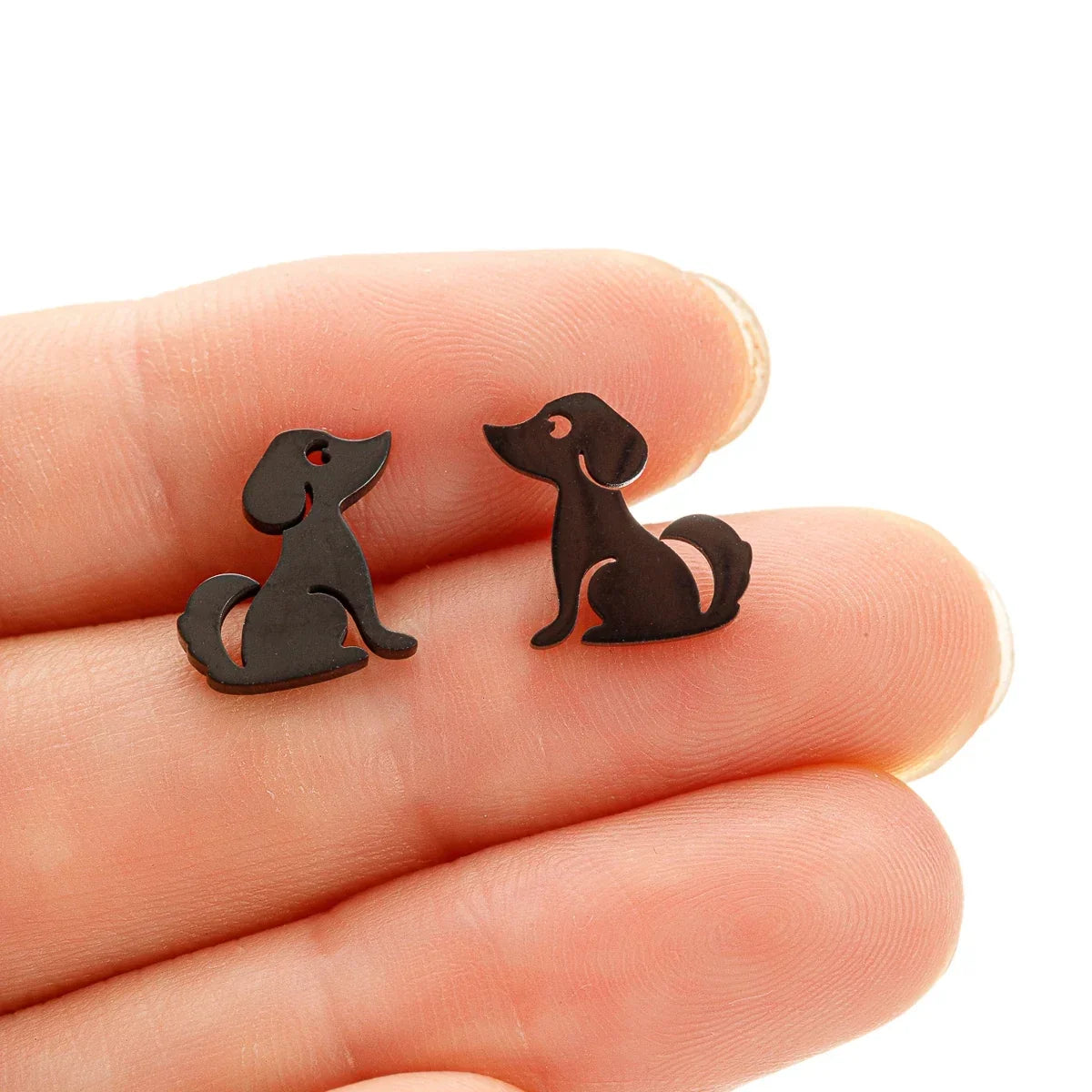 Black dog stud earrings held between fingertips, close-up view