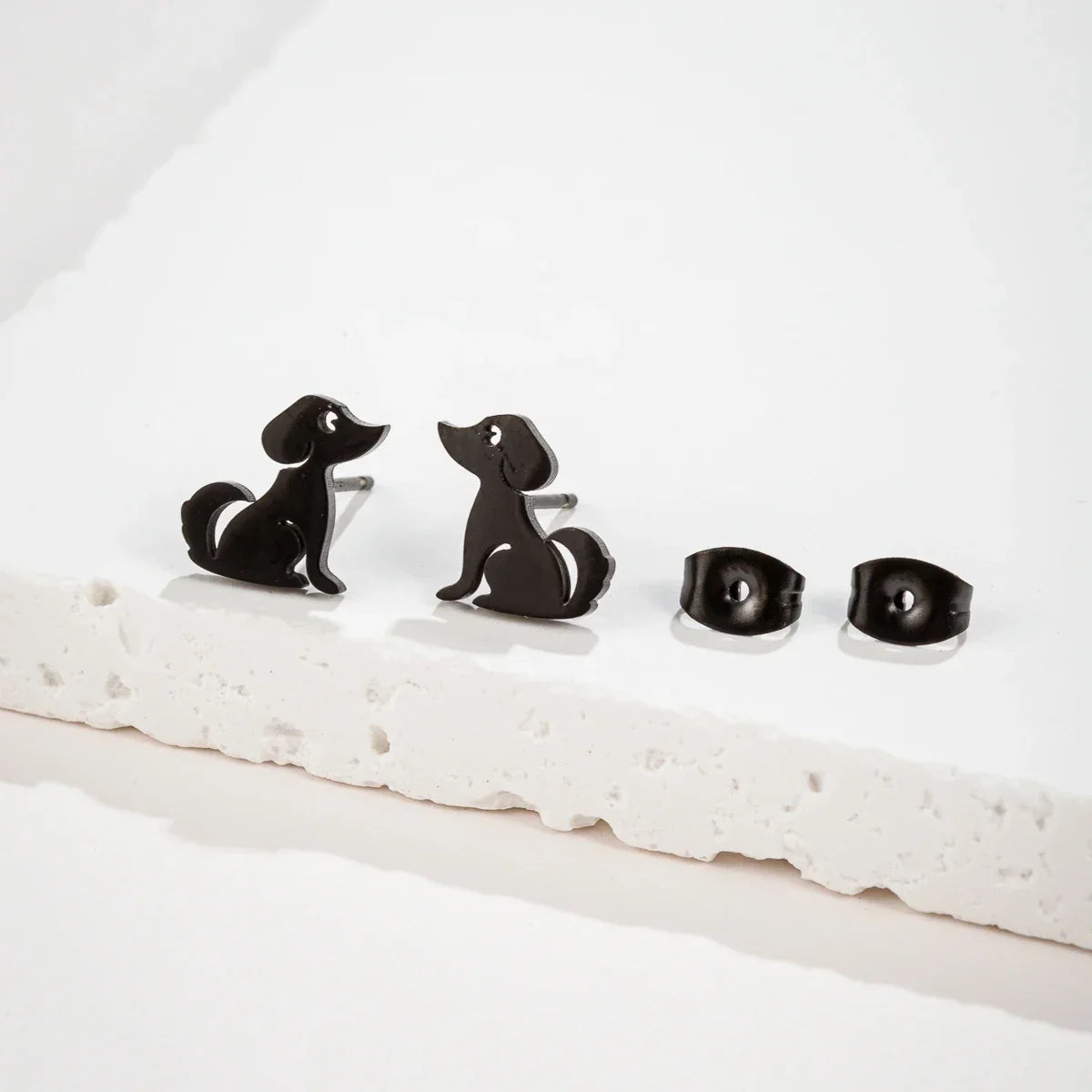 Black dog stud earrings with butterfly backs on a white surface