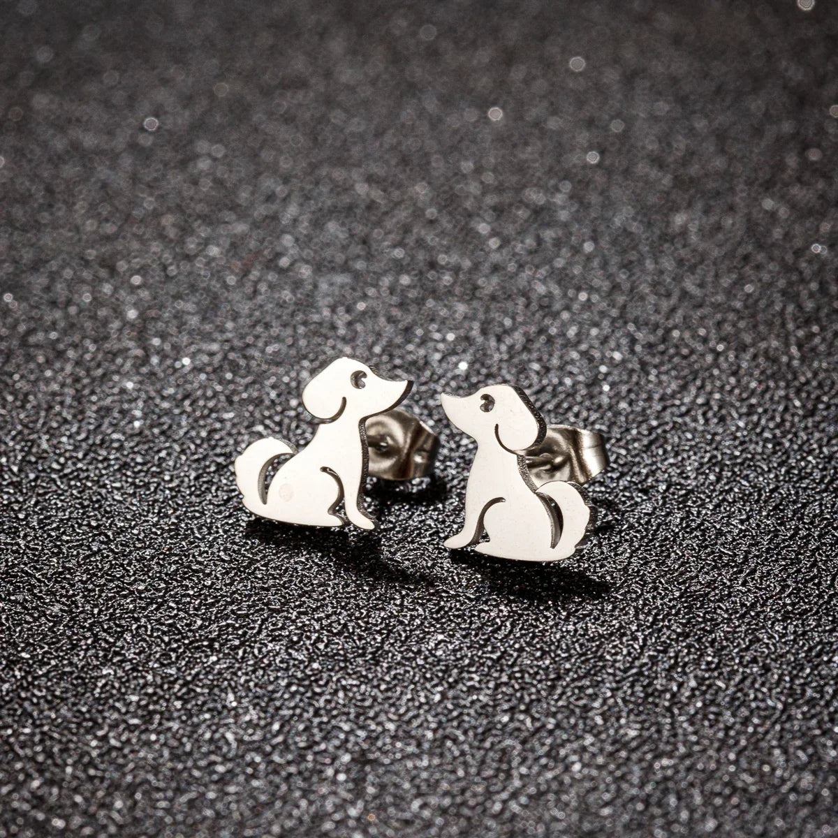 Silver sitting dog stud earrings on a dark textured background