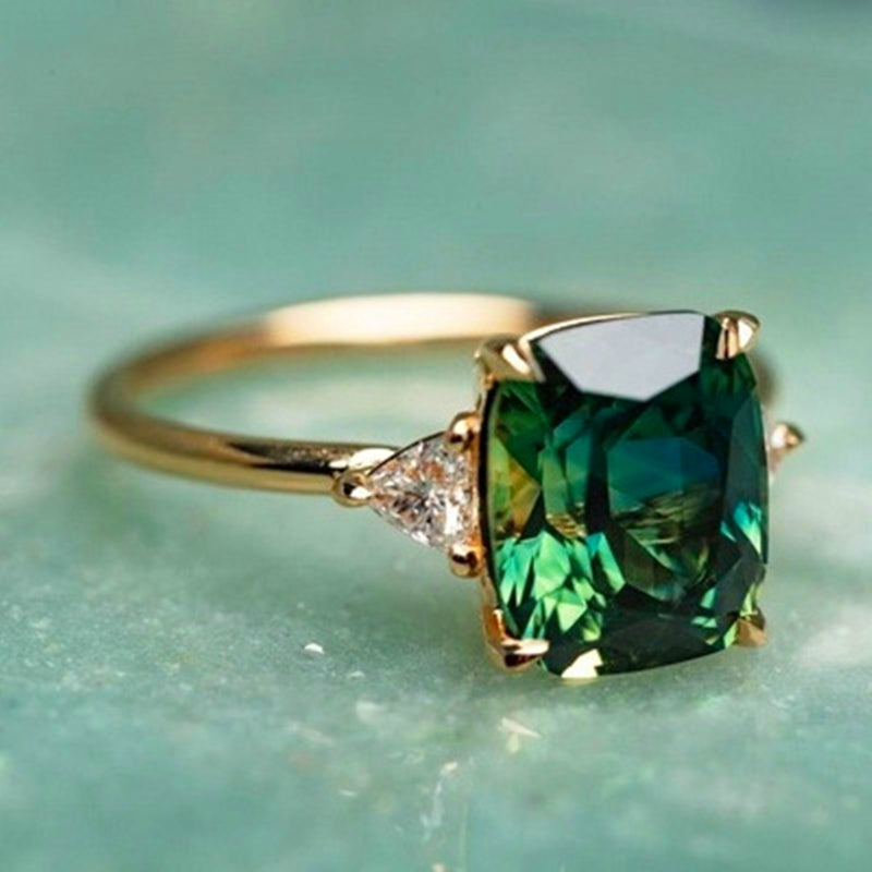 Green zirconia gold ring with cushion-cut stone and clear side stones, close-up view
