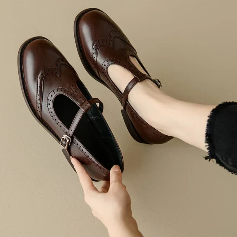 Miana T-strap Mary Janes in brown, held in hand showing brogue detail
