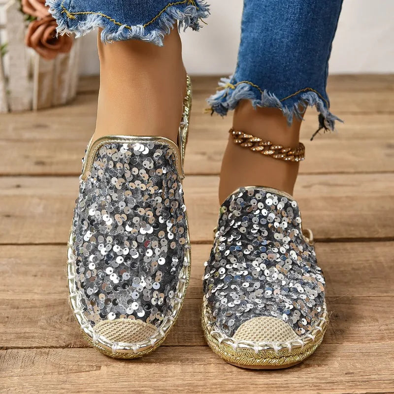 Sequinned slip-on flats in silver, worn front view with jeans