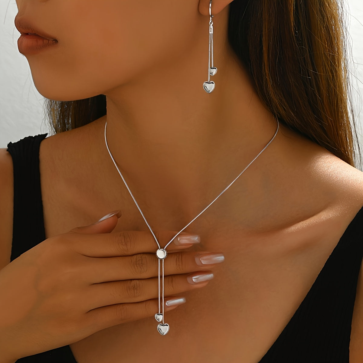Silver heart pendant necklace and drop earrings worn, close-up view