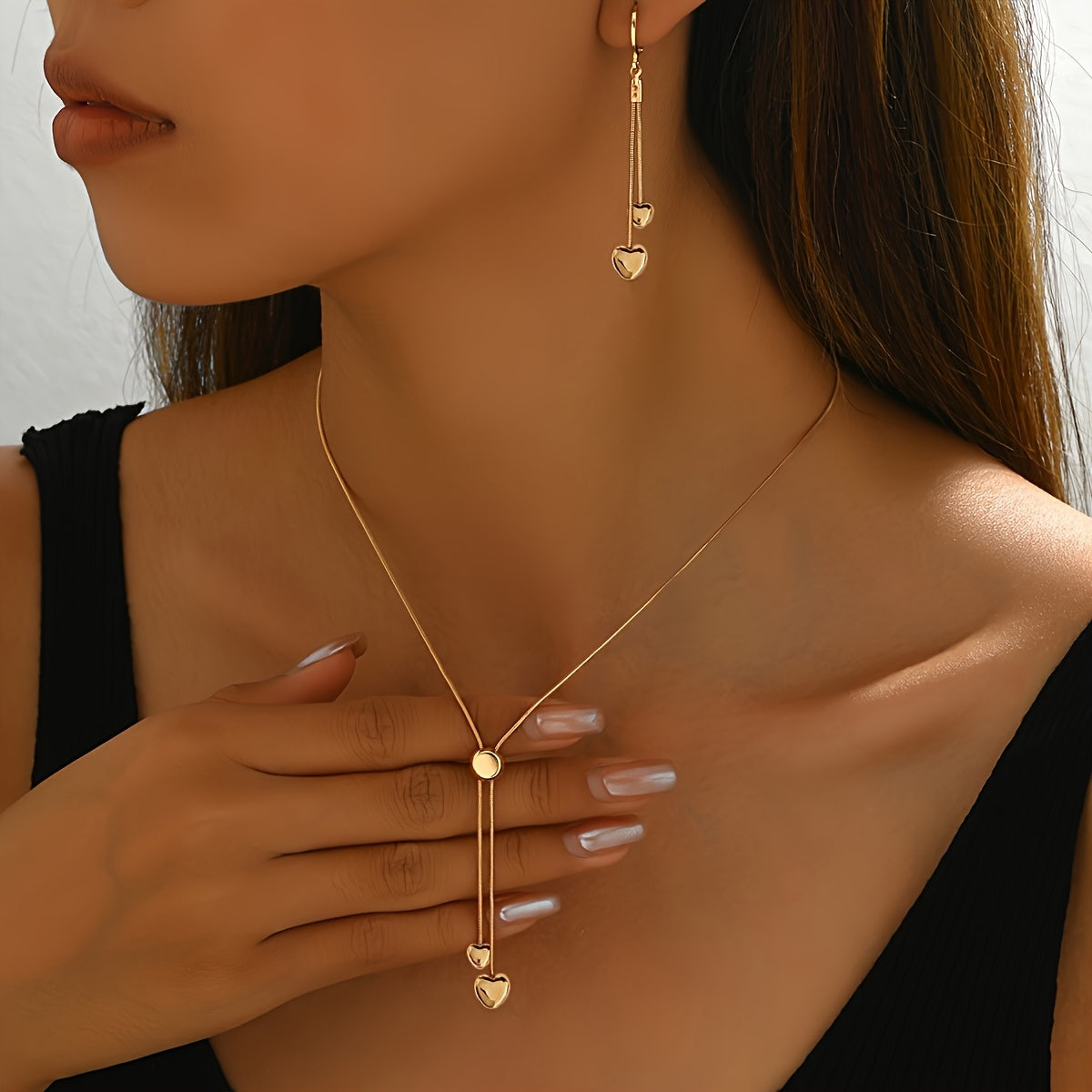 Gold heart pendant necklace and drop earrings worn on the neck, close-up view
