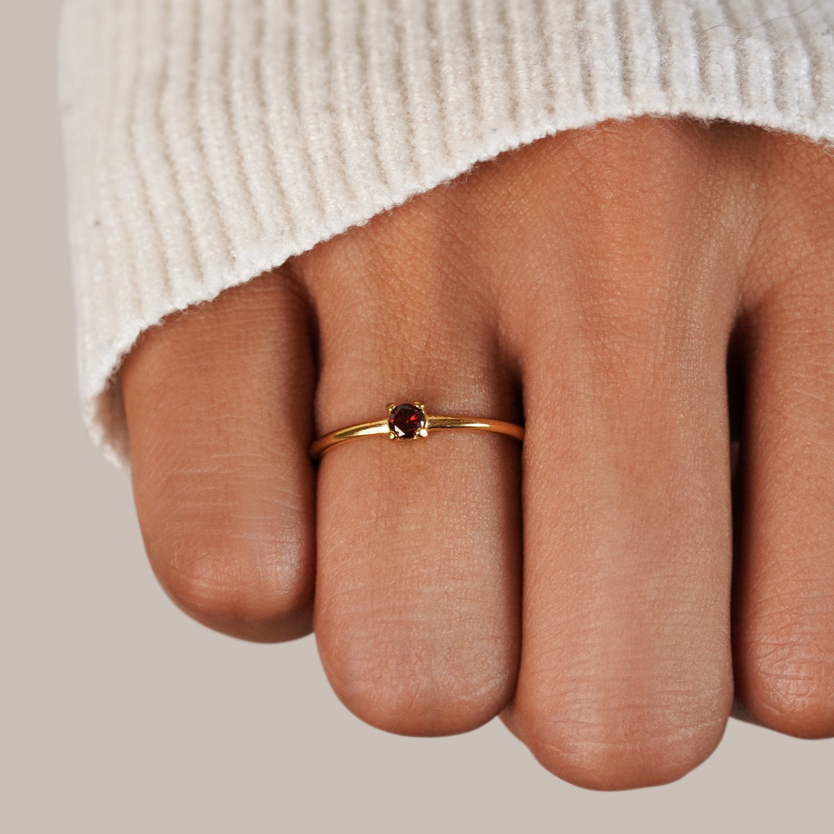 Gold birthstone ring with red garnet stone worn on the hand