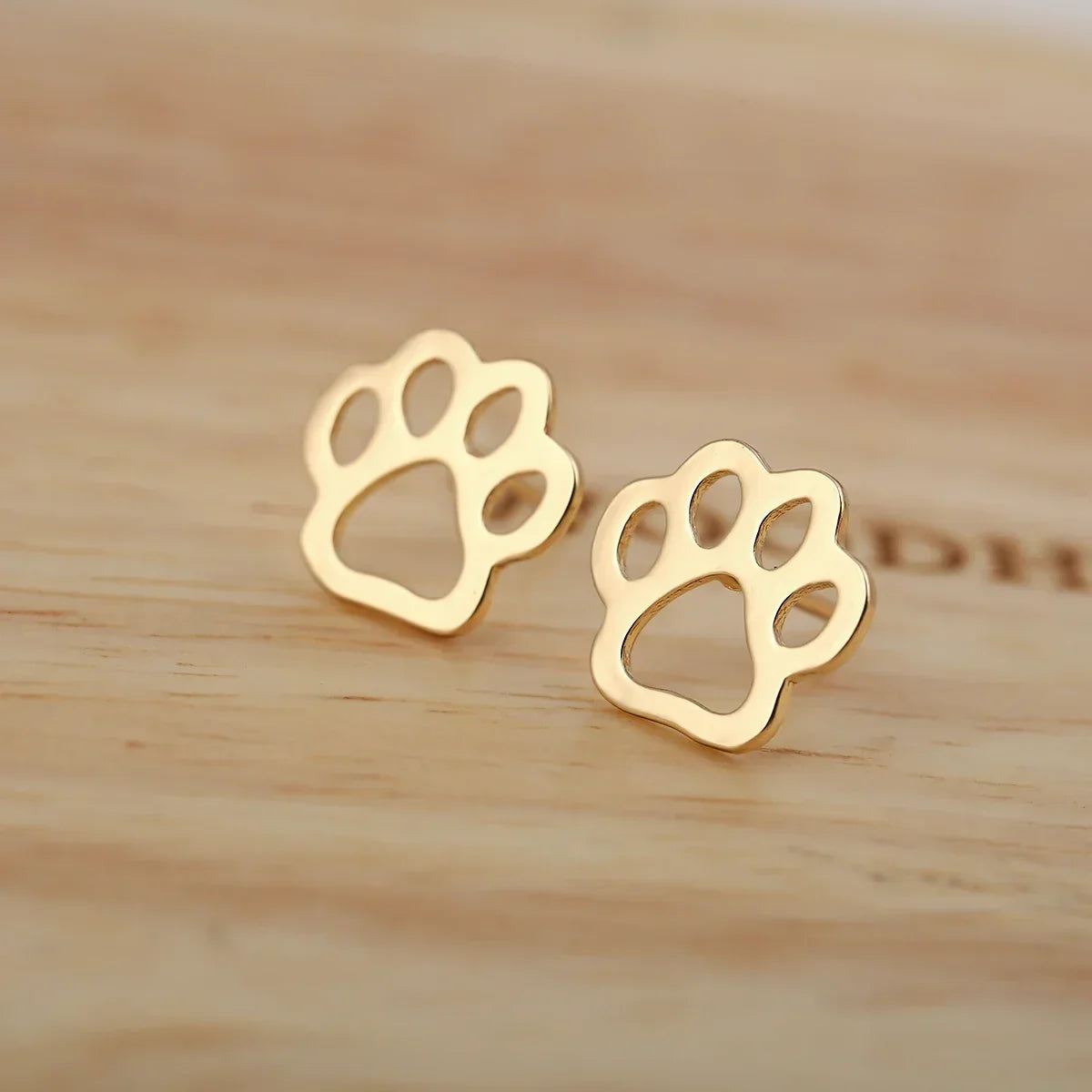 Pair of gold paw print stud earrings on a wooden surface