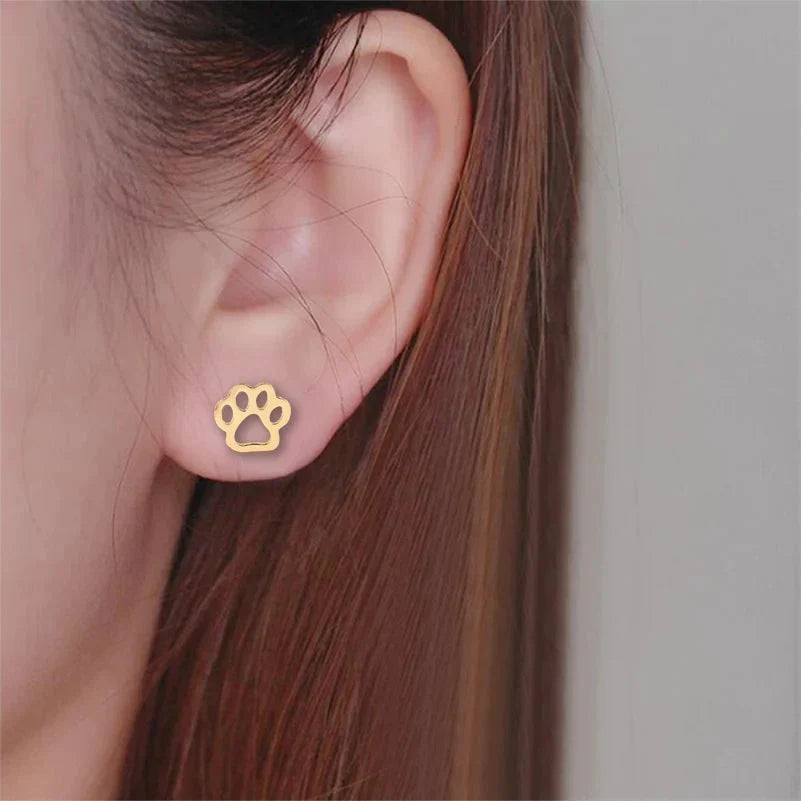Gold paw print stud earring worn on the ear, close-up side view