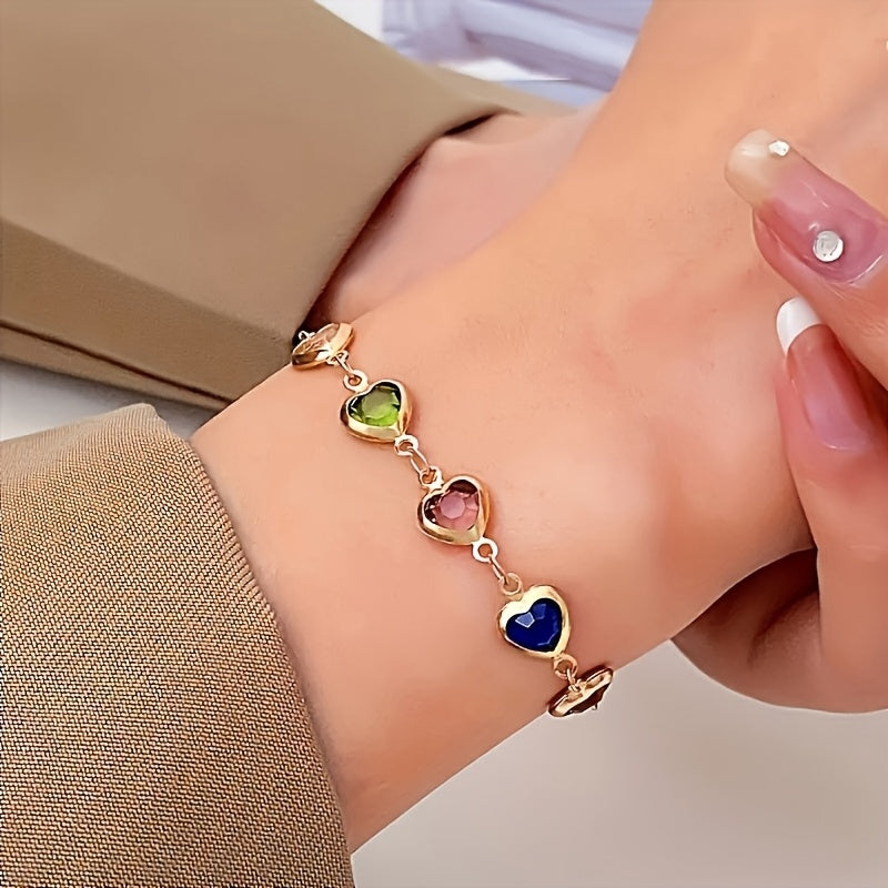 Gold heart bracelet with green, pink and blue stones worn on wrist
