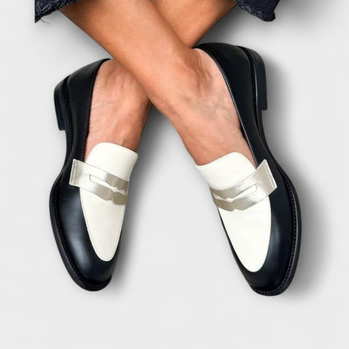 Iris loafers in black and ivory with gold strap, worn crossed at the ankles