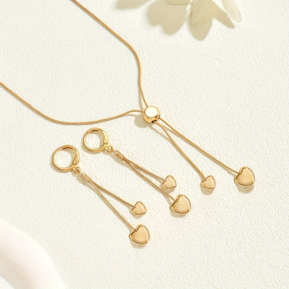 Gold heart necklace and earrings set styled flat on a cream surface