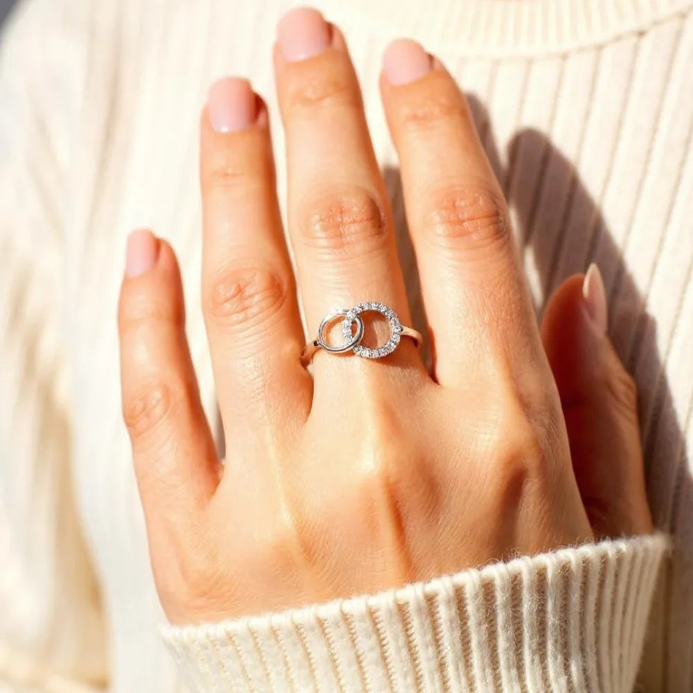 Silver interlinked circles ring worn on a hand resting on a cream jumper
