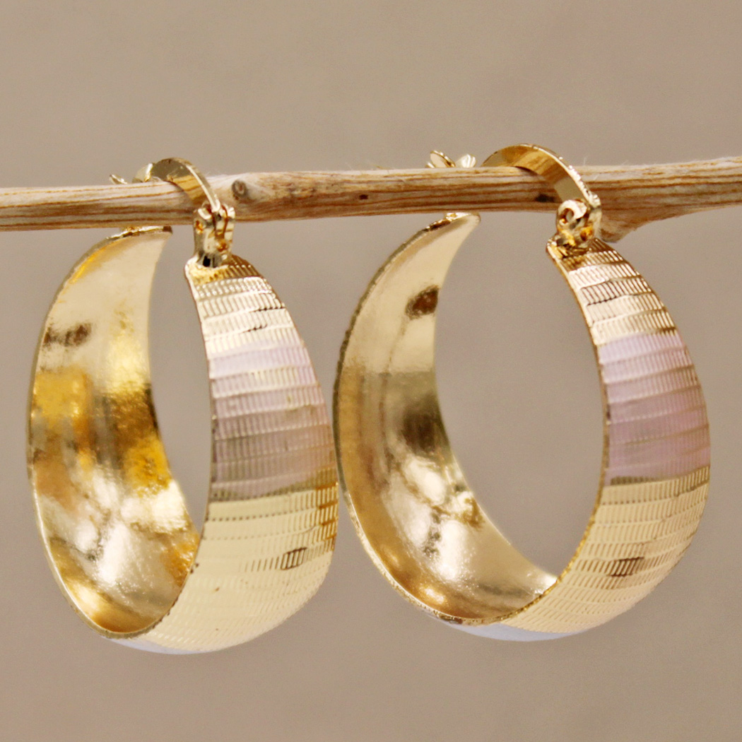Gold tapered hoop earrings with ribbed detail, side view on a branch