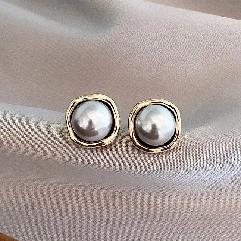 Pearl stud earrings with wavy gold-toned frames on soft fabric