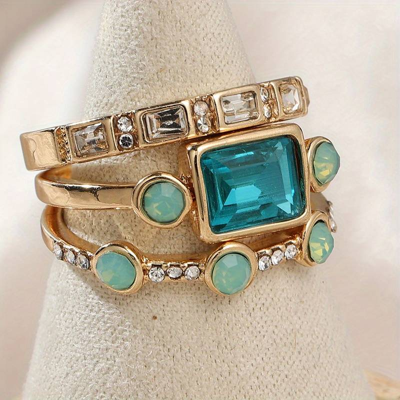 Blue crystal ring set in gold tone, three stacked bands shown on a display